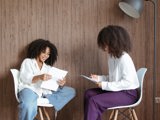 two light skinned women sitting down going though work